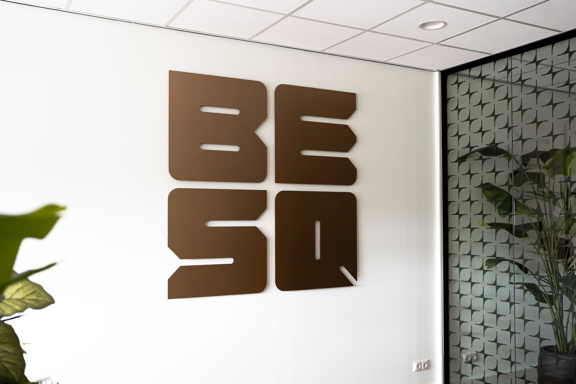 Het bruine, uitgesneden logo van BESQ Group bevestigd aan een witte muur in het kantoor.