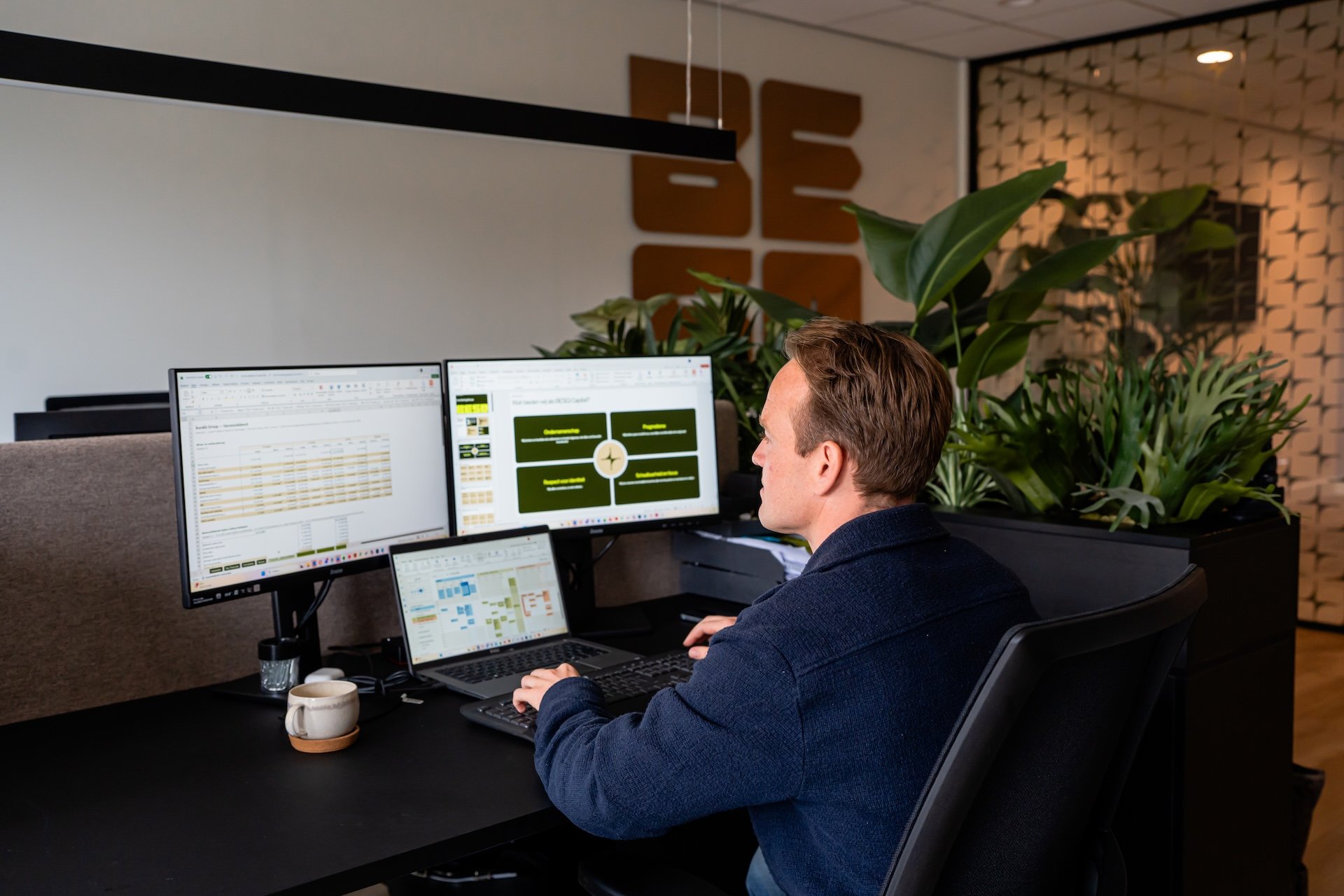 Mannelijke medewerker van BESQ Group aan het werk met spreadsheets en een dashboard-presentatie op meerdere beeldschermen.