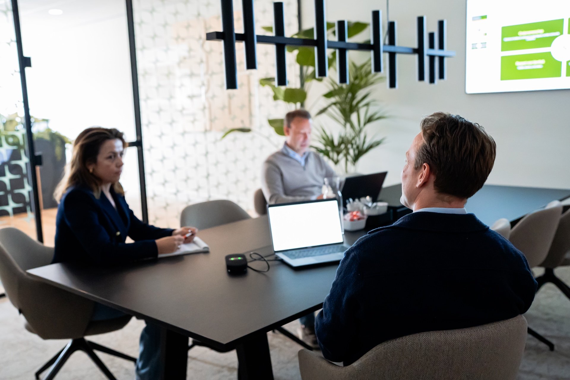 Drie collega's in overleg aan een vergadertafel op het kantoor van BESQ Group, met open laptops en aantekeningen.